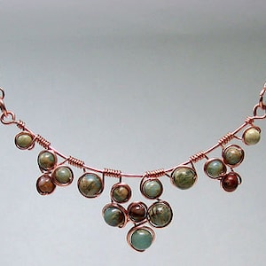 May include: A copper wire necklace with a cascading design of green and brown gemstone beads.