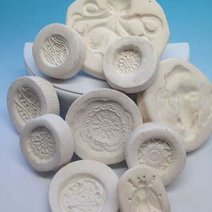 May include: A collection of white ceramic molds with various designs, including an octopus, flowers, and geometric patterns. The molds are perfect for creating unique and decorative items.