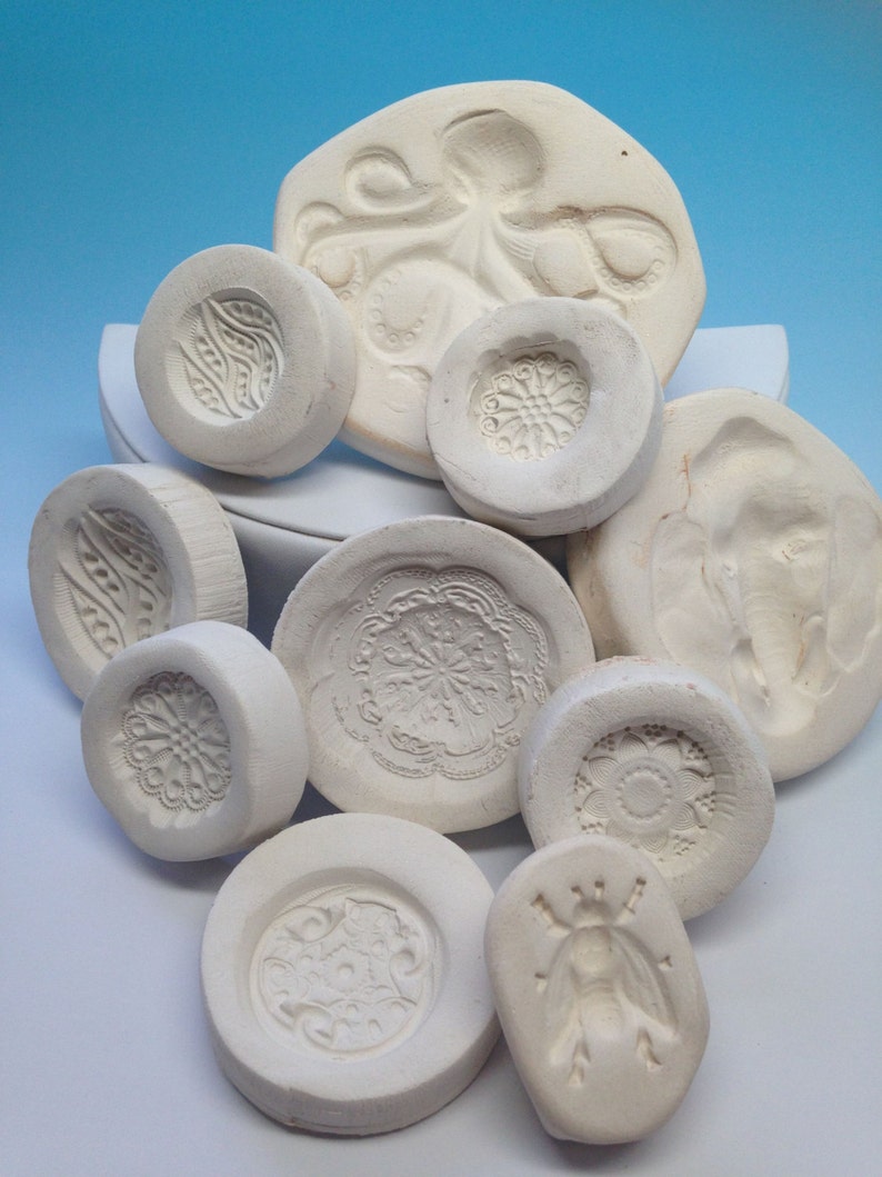 May include: A collection of white ceramic molds with various designs, including an octopus, flowers, and geometric patterns. The molds are perfect for creating unique and decorative items.