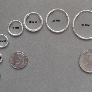 Op de afbeelding: Een set zilveren creolen in verschillende maten, variërend van 10 mm tot 40 mm in diameter. De oorbellen zijn in een halve cirkel gerangschikt, met de kleinste oorbellen onderaan en de grootste oorbellen bovenaan. Een Nederlandse 1-euro munt is opgenomen ter referentie van de grootte.