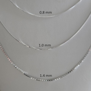 May include: Three silver box chain necklaces of different thicknesses are shown. The thinnest chain is labelled 0.8 mm, the middle chain is 1.0 mm, and the thickest is 1.4 mm. The necklaces are displayed on a white mannequin bust.