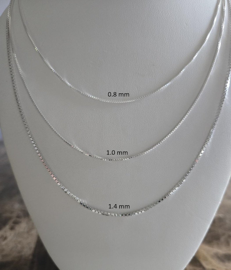 May include: Three silver box chain necklaces of different thicknesses are shown. The thinnest chain is labelled 0.8 mm, the middle chain is 1.0 mm, and the thickest is 1.4 mm. The necklaces are displayed on a white mannequin bust.