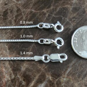 May include: Three silver box chains of varying thicknesses: 0.8 mm, 1.0 mm, and 1.4 mm. Each chain has a clasp. A coin is next to the chains for size comparison.