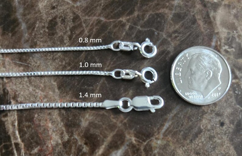 May include: Three silver box chains of varying thicknesses: 0.8 mm, 1.0 mm, and 1.4 mm. Each chain has a clasp. A coin is next to the chains for size comparison.