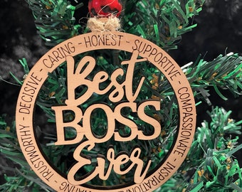 Może przedstawiać: Okrągła drewniana ozdoba z napisem Best BOSS Ever pośrodku, otoczona obwódką ze słowami Decisive, Caring, Honest, Supportive, Compassionate, Inspirational, Motivating oraz Trustworthy, zwieńczona dwoma koralikami.