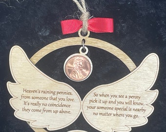 Może przedstawiać: Drewniana ozdoba w kształcie skrzydeł anioła z miedzianym groszem w środku. Ozdoba zawiera tekst "Heaven's raining pennies, from someone that you love. It's really no coincidence they come from up above." i "So when you see a penny pick it up and you will know, your someone special is nearby no matter where you go." Ozdoba jest spersonalizowana imieniem "Olivia".