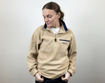 May include: A beige fleece pullover with a navy blue zipper and trim. The pullover has the text "Team 9" embroidered on the front.