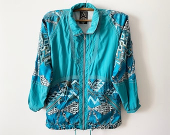 May include: A turquoise blue jacket with a geometric pattern in shades of blue, white, and black. The jacket has a zipper closure and a drawstring at the bottom.