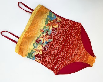 Peut inclure: Un maillot de bain rouge et jaune avec un imprimé floral et un motif en zigzag. Le maillot de bain a des bretelles fines et un décolleté arrondi.