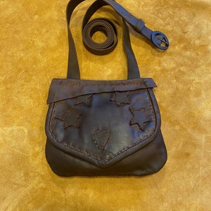May include: A brown leather satchel bag with a heart and star cutouts. The bag has a long strap with a buckle.