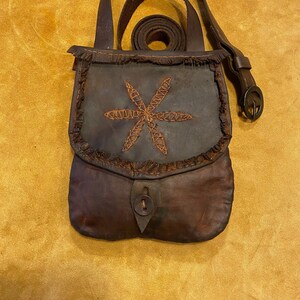 May include: A brown leather bag with a fringed flap and a star-shaped design. The bag has a strap and a button closure.