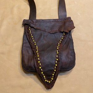 May include: A brown leather bag with a fringe detail and yellow beads. The bag has a long strap and a buckle closure.