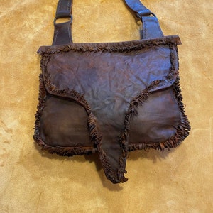 May include: A brown leather satchel with a fringed edge and a long strap. The strap has a buckle and is rolled up.