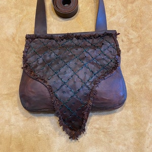 May include: A brown leather bag with a fringed flap and a green stitched design. The bag has a long brown leather strap.