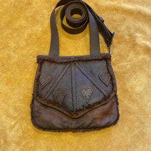 May include: A brown leather satchel with a fringe trim and heart-shaped cutouts. The bag has a long adjustable strap.