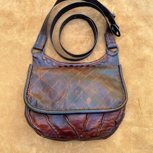 May include: A brown leather satchel with a flap closure and a long adjustable strap. The bag has a quilted design and is distressed for a vintage look.