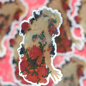 May include: A sticker featuring a nude figure with a floral design. The flowers are red, orange, and yellow, and they cover the figure's body. The sticker is on a pink background.