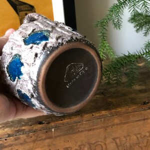 May include: A brown ceramic mug with a textured surface and blue glaze. The mug has a handle and a round base. The bottom of the mug has a black stamp that reads "Made in China".