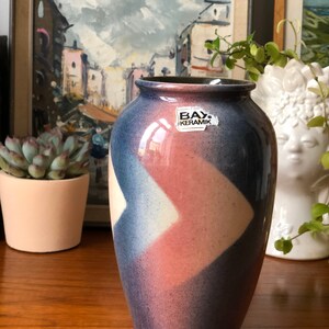 Könnte beinhalten: Eine blaue und rosafarbene Keramikvase mit geometrischem Muster. Die Vase trägt ein Etikett mit der Aufschrift "BAY Keramik".