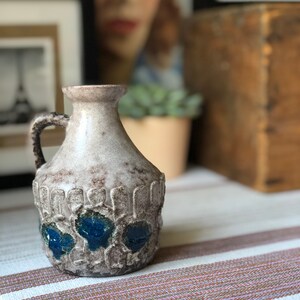 May include: A ceramic vase with a textured surface and blue and white glaze. The vase has a rounded body and a narrow neck with a handle.