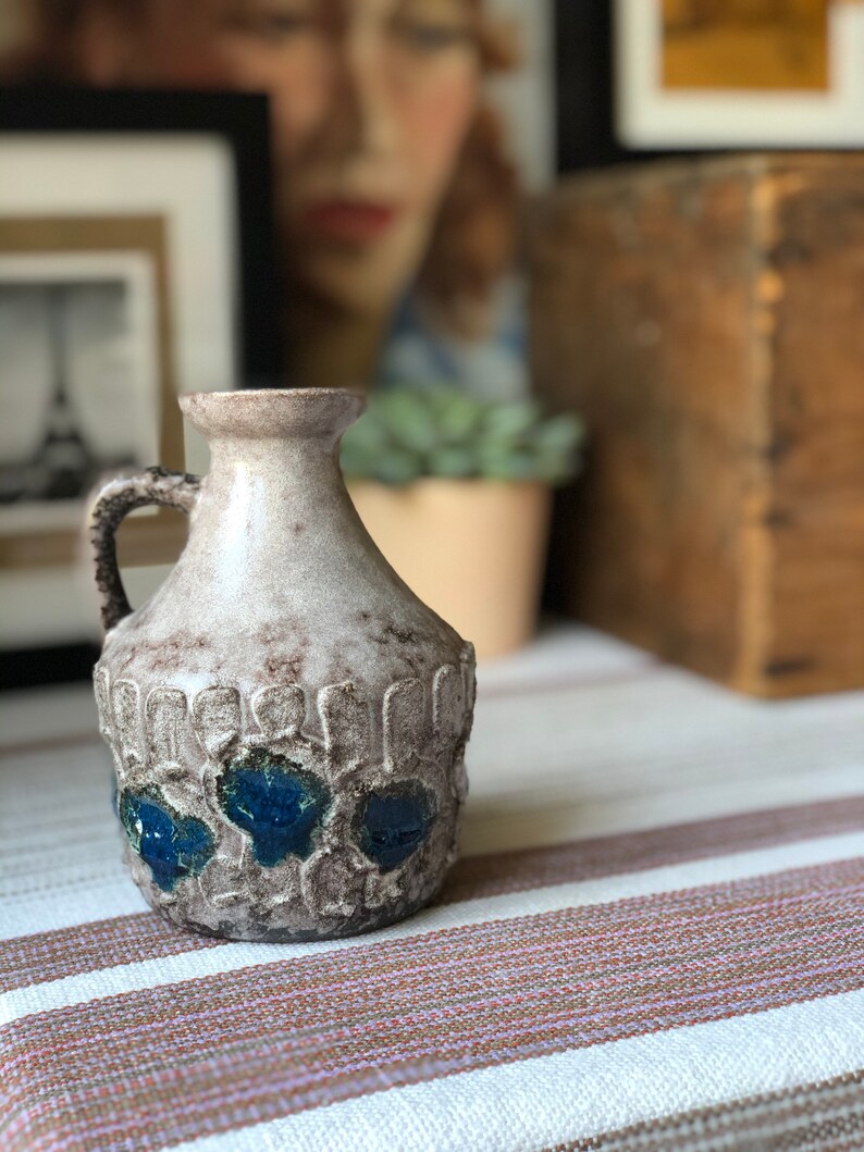 May include: A ceramic vase with a textured surface and blue and white glaze. The vase has a rounded body and a narrow neck with a handle.