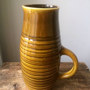 May include: A brown ceramic jug with a ribbed design and a handle. The jug is glazed and has a glossy finish.