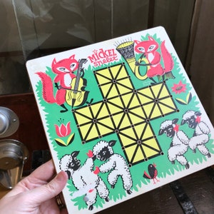 Puede incluir: Un tablero de juego colorido con un patrón de cuadrícula e ilustraciones de zorros, pájaros y un instrumento musical. El juego se llama "Mickel Snelet".