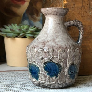 May include: A gray ceramic pitcher with a textured surface and blue floral designs. The pitcher has a handle and a spout.