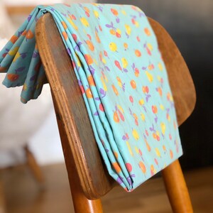 Puede incluir: Una tela azul doblada con un patrón de fruta amarilla, naranja y morada en una silla de madera.