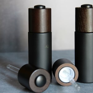 May include: Three black glass bottles with brown wooden caps and droppers. The bottles are on a gray surface.
