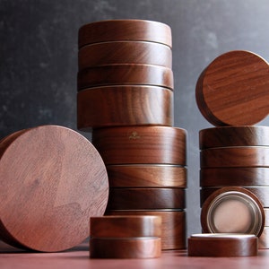 Puede incluir: Colección de recipientes redondos de madera apilados con tapas. Los recipientes son de un rico color marrón oscuro, con vetas de madera visibles. Algunos están abiertos, revelando un interior plateado. Ideal para almacenamiento o exhibición.