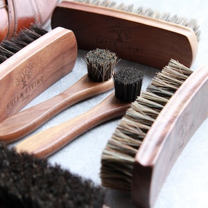 Könnte beinhalten: Ein Set aus vier Schuhbürsten mit Holzgriffen. Die Bürsten haben verschiedene Formen und Größen und bestehen aus Naturborsten. Die Griffe sind mit den Worten "Green Living Shop" graviert.