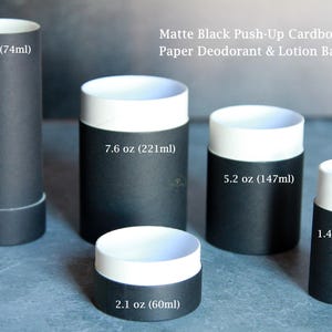 May include: Matte black push-up cardboard tubes for paper deodorant and lotion bar packaging in various sizes: 2.5 oz (74ml), 7.6 oz (221ml), 5.2 oz (147ml), 1.4 oz (42ml), and 2.1 oz (60ml). These cylindrical containers feature white inner rims.