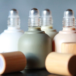 May include: A collection of roll-on bottles in various colors, including white, green, and peach. The bottles have silver rollerball applicators and are accompanied by wooden caps. The design is simple and elegant, suitable for essential oils or perfumes.