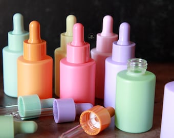 May include: Seven pastel colored glass dropper bottles with clear glass droppers. The bottles are arranged in a row on a wooden surface. The colors of the bottles are light blue, orange, yellow, pink, light purple, green, and lavender.