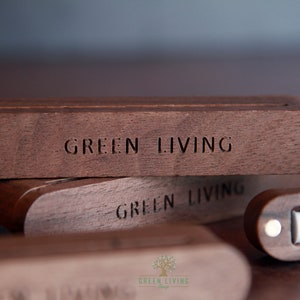 Puede incluir: Primer plano de tres cajas de madera apiladas una encima de la otra. La caja superior tiene las palabras "GREEN LIVING" grabadas en la parte delantera. Las cajas son de madera marrón oscura.