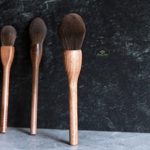 Puede incluir: Cuatro cepillos con mango de madera y cerdas naturales. Los cepillos están dispuestos en una fila sobre una superficie gris.