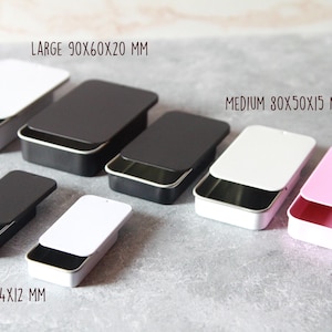 May include: Rectangular metal tins in various sizes and colors, including white, black, and pink. The largest tin measures 90x60x20 mm, the medium is 80x50x15 mm, and the smallest is 60x34x12 mm. Each tin has a matching lid.