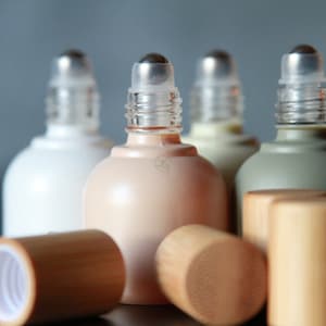 May include: Five glass roller bottles with metal roller balls and wooden caps. The bottles are in various colors, including white, beige, and green.