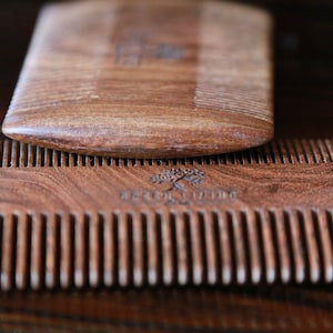 May include: Two wooden combs, one on top of the other. The top comb is plain, while the bottom comb has a tree design and the text "GREEN LIVING" engraved on it.