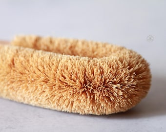 May include: Close-up of a natural bristle brush with a wooden handle. The bristles are made of coconut fibers and are a light brown color.