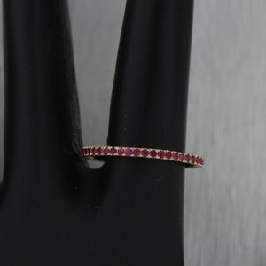May include: A thin gold band ring with a row of small, red ruby stones.