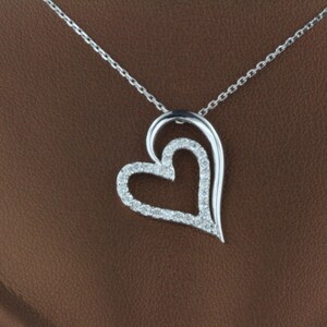 May include: A silver necklace with a double heart pendant. The pendant is made of two interlocking hearts, both of which are encrusted with small, clear gemstones.