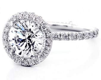 Könnte beinhalten: Ein silberner Verlobungsring mit einem großen runden Diamanten in der Mitte, der von einem Heiligenschein aus kleineren Diamanten umgeben ist. Die Ringschiene ist ebenfalls mit kleineren Diamanten besetzt.