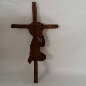 May include: A wooden cross with a carved silhouette of a person kneeling in prayer. The cross is dark brown and the figure is in a praying position.
