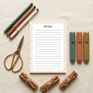 May include: A rectangular notepad with the word Notes printed at the top, featuring horizontal lines and a light orange leaf border. Included are three pens, three markers, gold-toned scissors, and three bundles of cinnamon sticks.