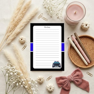 May include: A rectangular notepad with a white lined center, black borders, and a blue horizontal stripe on each side. The top is labeled Notes in black text, and a small illustration of a blue and black police car is at the bottom right.