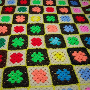 May include: A crocheted blanket with a checkered pattern in various colors, including pink, blue, green, yellow, and red.