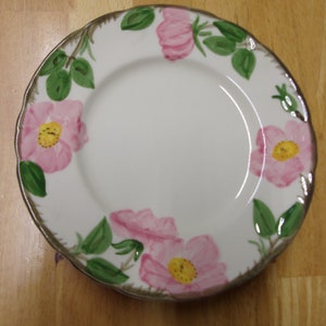 May include: A white ceramic plate with a scalloped edge features a floral design of pink roses with green leaves. The roses have yellow centers.