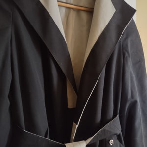 May include: A black coat with a white lining and a contrasting black trim. The coat has a large collar and a belt.